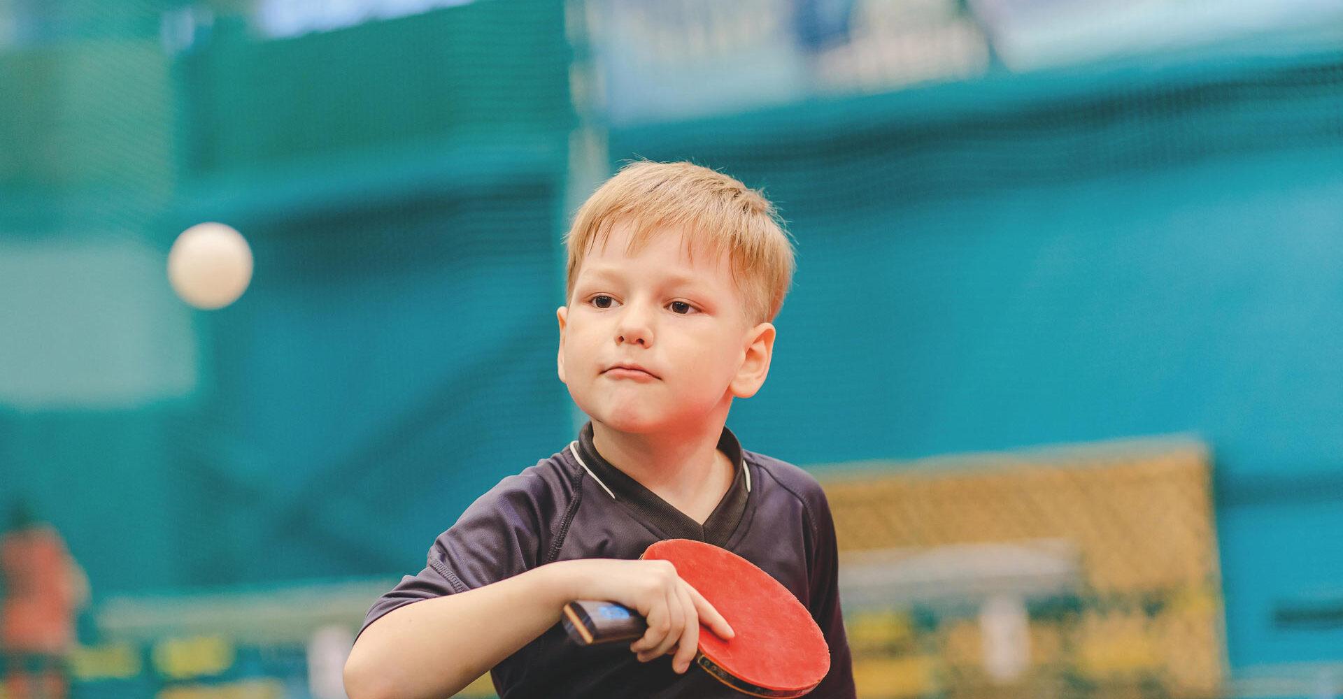 Junge mit Tischtennisschläger in der Hand schaut konzentriert auf einen Ball, der ihm entgegenfliegt.
