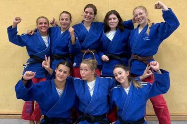 Gruppenbild von acht Judokas in blauen Anzügen mit unterschiedlichen Gürtelfarben, alle lächeln und posieren.