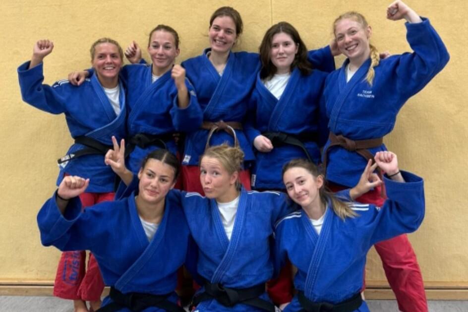 Gruppenbild von acht Judokas in blauen Anzügen mit unterschiedlichen Gürtelfarben, alle lächeln und posieren.