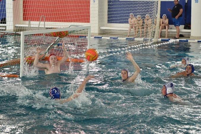 Wasserballspiel: Spieler werfen einen Ball auf das Tor, während der Torwart zum Abwehren bereit ist.