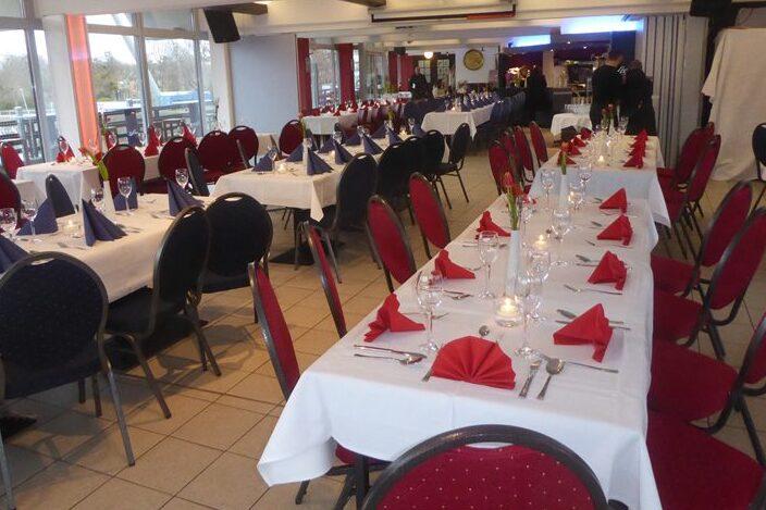 Elegant dekorierter Restaurantbereich mit weiß eingedeckten Tischen und roten sowie blauen Servietten.